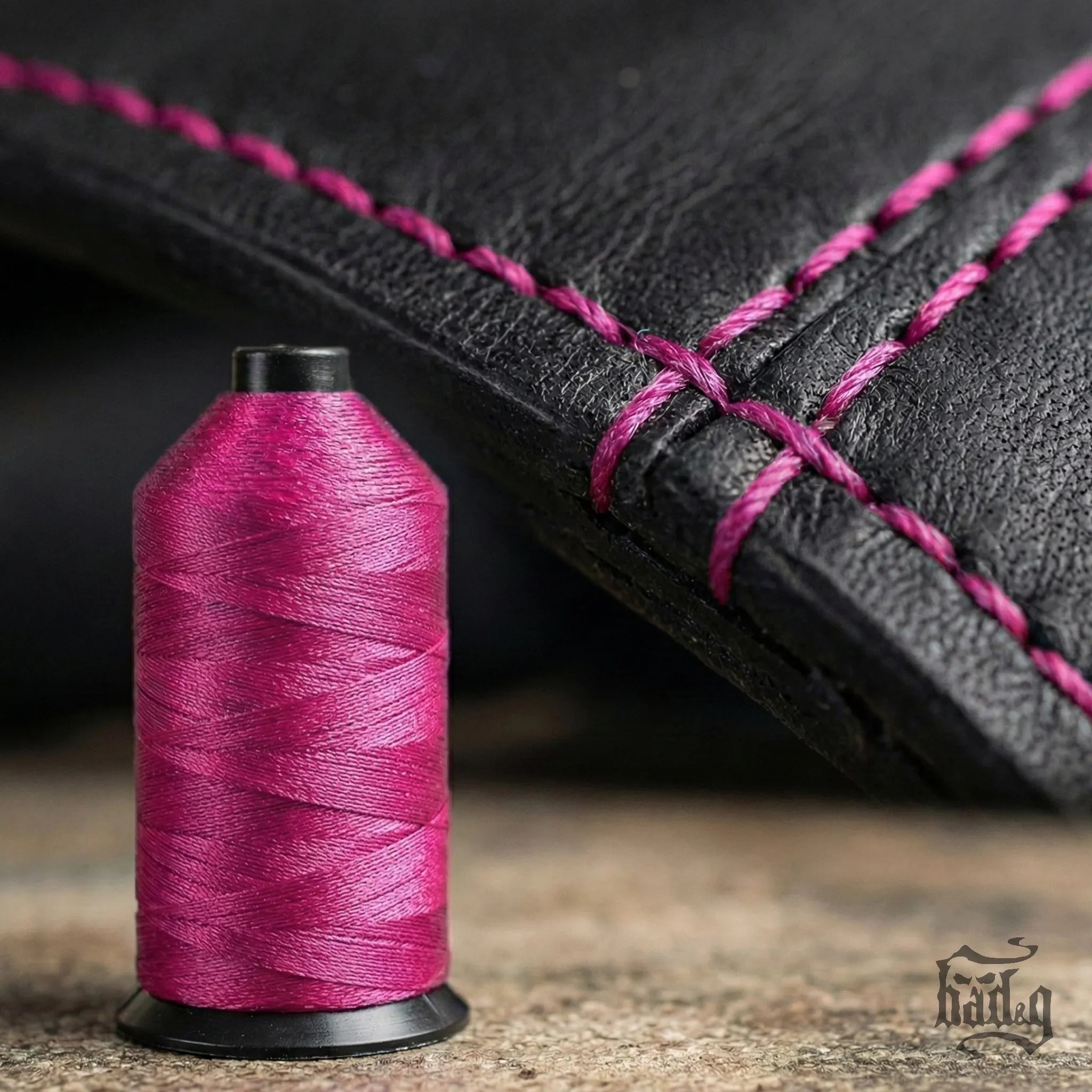Spool of pink thread next to a black leather product with pink stitching